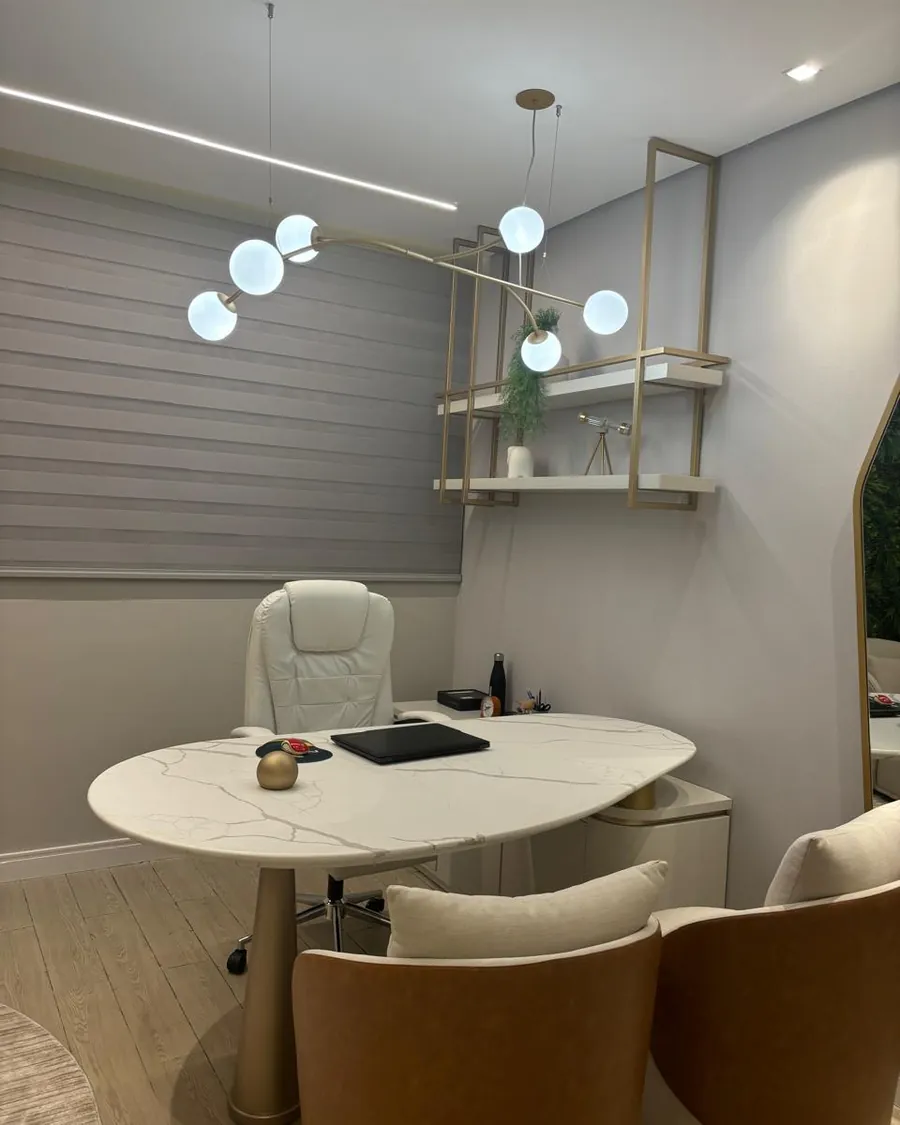Sala de atendimento com mesa de mármore claro, poltronas e luminárias