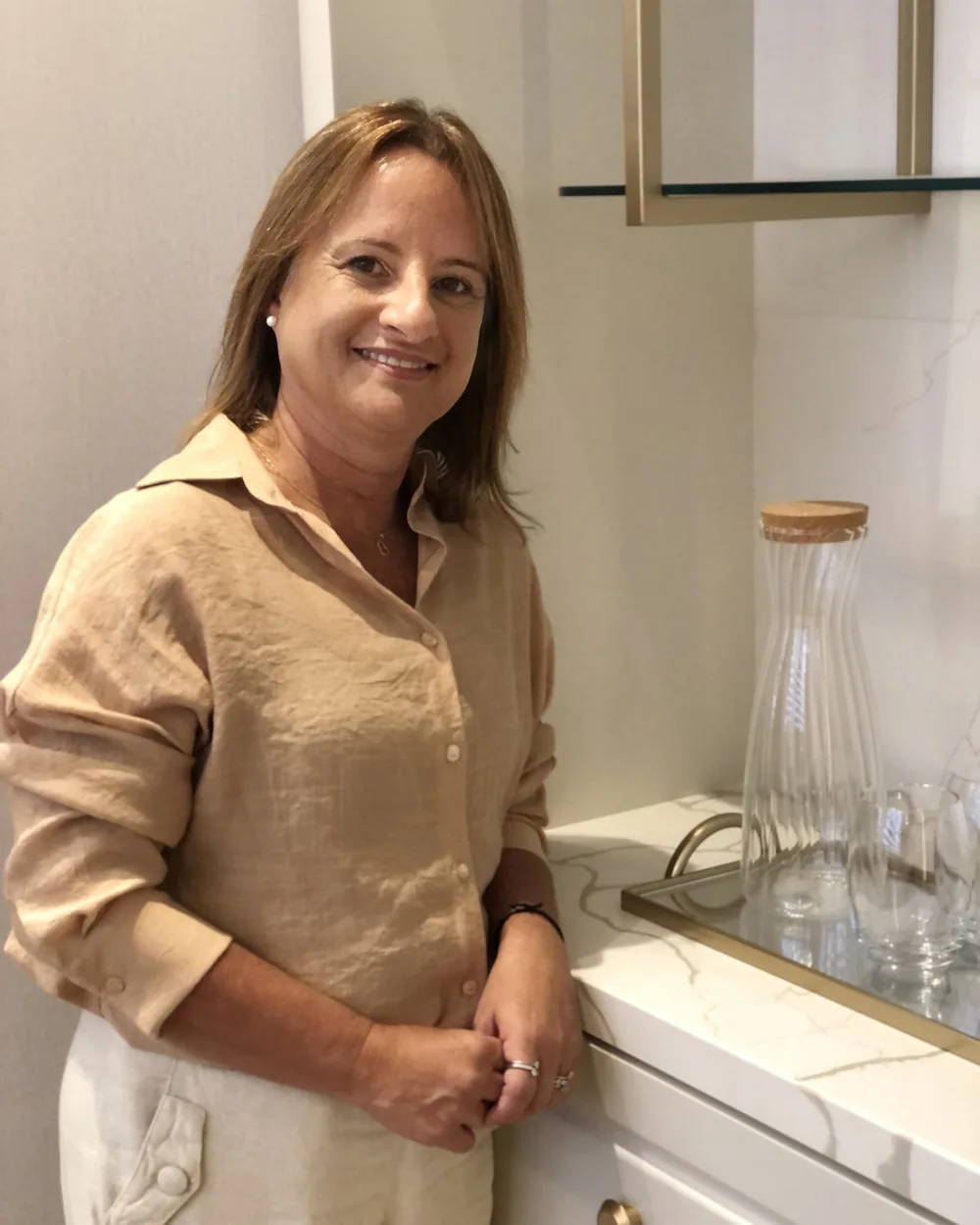 Adriana Assis de camisa bege, sorrindo, apoiada na bancada clara do consultório